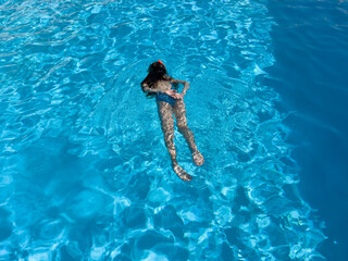 Girl swims in the pool with blue water.