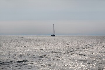 Lonely sailing boat on silver surface of water on horizon of sea