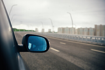 Black wing mirror of modern car. Left side car rear-view mirror and empty highway.