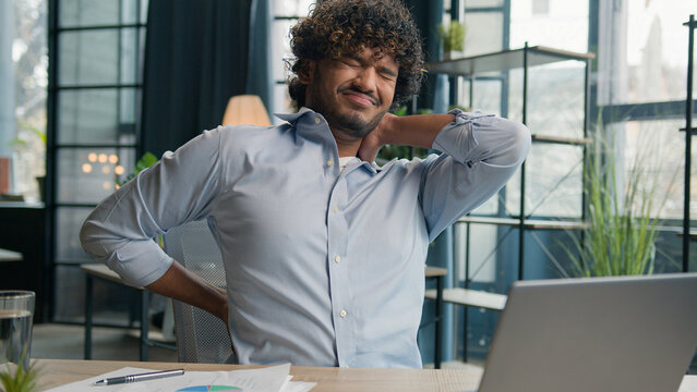 Sick exhausted Arabian Indian latino man feel pain in lower back backache after laptop work unwell ill male guy office manager massaging painful neck relieve ache health problem office syndrome injury