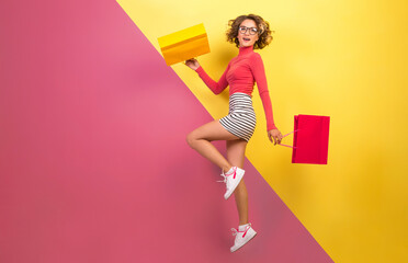 smiling attractive woman in stylish colorful outfit jumping with shopping bags