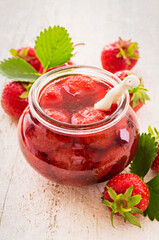 Ripe red strawberry from organic cultivation and marmalade offered as a close-up in a fruit jar on a wooden board