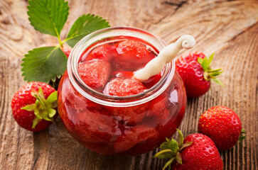 Ripe red strawberry from organic cultivation and marmalade offered as a close-up in a fruit jar on a wooden board