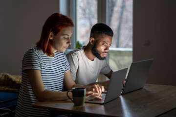 Serious man and woman working on laptops. Focused remote multiracial freelancer workers enthusiastically concentrate on online internet working at computer from home together jointly, typing.