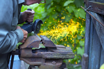 old man working. Cutting a metal pipe. spark. the pipe is clamped in a vice. man's hands hold a...