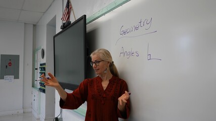 Wide angle view of woman teacher using an interactive whiteboard blackboard in an empty classroom teaching geometry math.