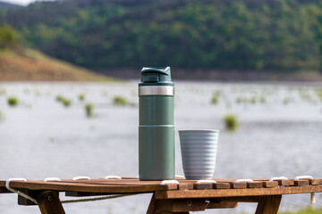 Isolated Stanley thermos without logo. Steel thermos for hot drinks at the camping table by the lake.  - obrazy, fototapety, plakaty