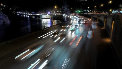 Busy road traffic on the bridge across the river in night city filmed in timelapse. Navigating on highway through urban landscapes. Blur of driving auto lights and changing rhythm of the downtown.