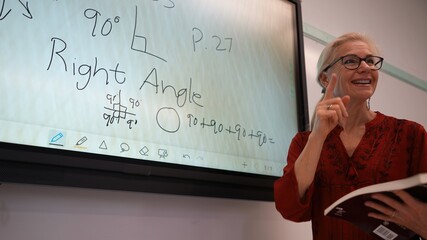 Closeup of happy female teacher writing on an interactive whiteboard teaching geometry math in a school classroom.