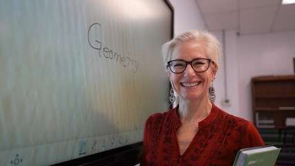 Closeup of smiling happy female teacher writing on an interactive whiteboard teaching geometry math in a school classroom.