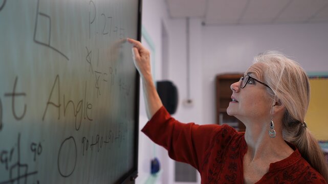 Closeup of happy female teacher writing on an interactive whiteboard teaching geometry math in a school classroom.