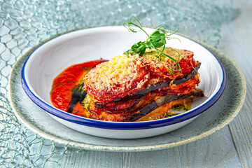 Eggplant baked with zucchini, carrot puree, pike perch, and vegetables in sauce on a blue background. Mediterranean Kitchen. Sea mood menu.