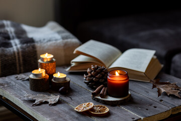 Cozy autumn or winter composition with aromatic candle, wool sweater, book. Aromatherapy, home atmosphere of cosiness and relax. Wooden background close up.