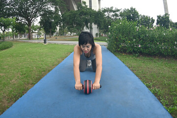 Pretty Asian woman with sports roller standing on her knees and stretching forwards on the floor...