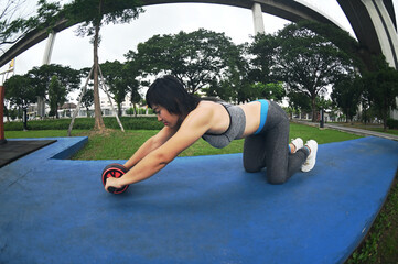 Pretty Asian woman with sports roller standing on her knees and stretching forwards on the floor...
