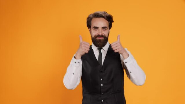 Confident worker does thumbs up sign, acting positive and cheerful in studio. Restaurant personnel showcasing okay symbol on camera, posing with confidence. waiter showing agreement gesture.