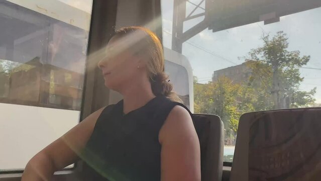 The girl sits and rides in the bus, she looks out the window Cityscape, public transport, woman near the window. She goes to work by bus. Weekdays, nice sunny weather.