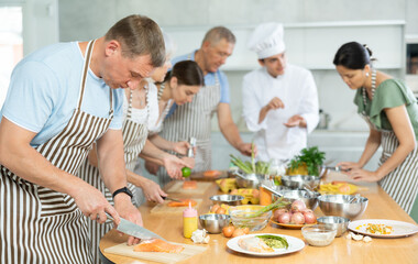 Adult man in apron learning to cook at cooking master class
