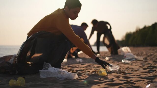 Earth day. Volunteers activists collects garbage cleaning of beach coastal zone. Woman and mans puts plastic trash in garbage bag on ocean shore. Environmental conservation coastal zone cleaning