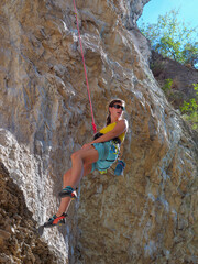 LOW ANGLE VIEW: Lady hangs on rope after failed attempt of climbing an overhang