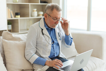 Senior man doctor working with laptop computer. Professional senior mature healthcare expert searching information or have online consultation in hospital room. Medicine healthcare medical checkup
