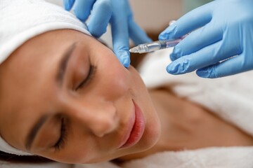 Closeup of young woman receiving hyaluronic acid injection in cheekbones at beauty salon.