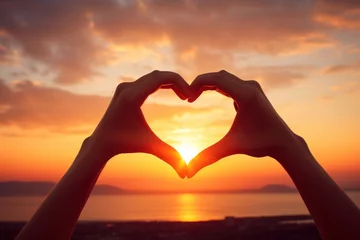Fototapete Orange Hands forming a heart shape against the backdrop of a sunset by the sea