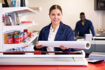 Friendly woman worker at printing house offering paper roll for plotter