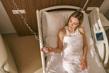 Young woman patient holding emergency call button while lying in hospital bed. High quality photo