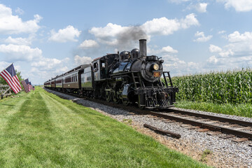 Strasburg, Pennsylvania – August 2023: Strasburg Steam Train rides along though corn fields in...