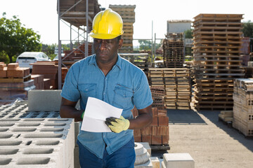 Focused african american man manager, keeps records of construction materials in an open air...