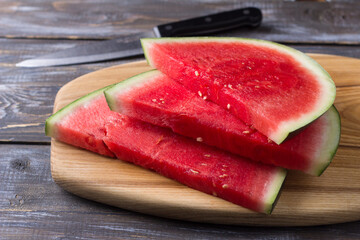 Seedless watermelon, slices on a wooden board with a knife and half of a watermelon on a wooden background