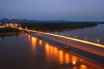 Aerial view of Thai Laos bridge with Mekong River with green mountain hill at night. Nature landscape background in Ubon Ratchathani, Thailand.