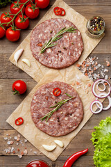 Raw burger patties on parchment and hamburger ingredients on wooden background, top view