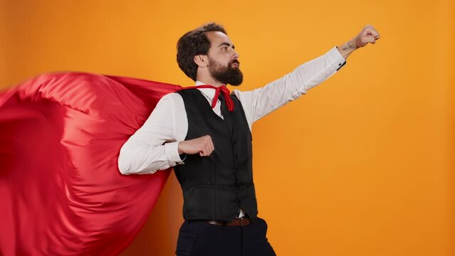 Powerful hero butler posing with red cape against yellow background, dedicated to serve consumers at fine dining restaurant. Concept of strong confident superhero character, luxury catering.