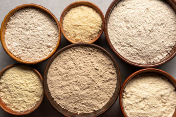 Set of organic flour in clay bowls on gray background