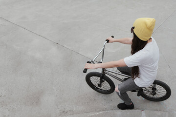 cool young woman sitting on a freestyle bike in a skatepark looking straight ahead, from above