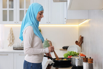 Muslim woman cooking dish in frying pan on cooktop indoors