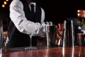 Bartender preparing fresh alcoholic cocktail in martini glass at bar counter, closeup