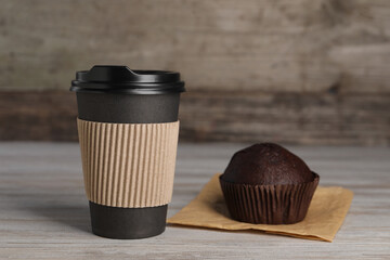 Paper cup with black lid and muffin on wooden table. Coffee to go