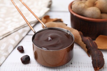 Measuring cup with tasty tamarind sauce and fresh pods on white wooden table, closeup