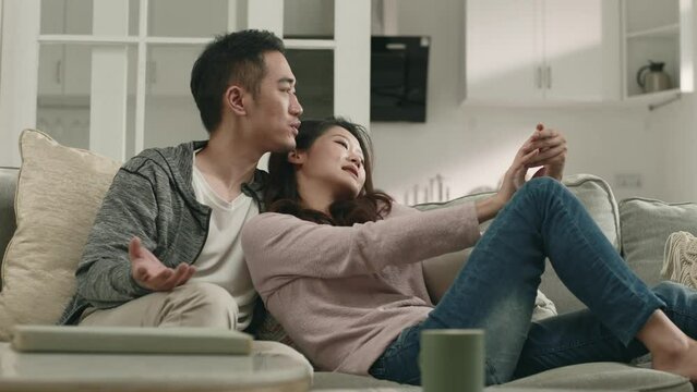 loving asian couple sitting on family couch at home having a conversation