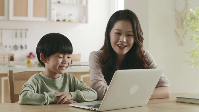 young asian mother watching movie at home with son using laptop computer