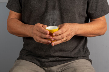 Hands of an elderly man holding a mug with a hot drink