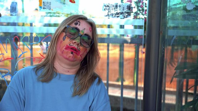 Woman with abstract makeup, painted face is sleeping at bus stop, car are reflected in window Contemporary art, social experiment street performance Tired children animator after shift April Fools Day