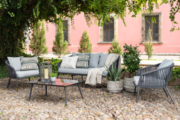 Outdoor boutique hotel patio in the garden with a grey sofa set with pillows and chairs on a...