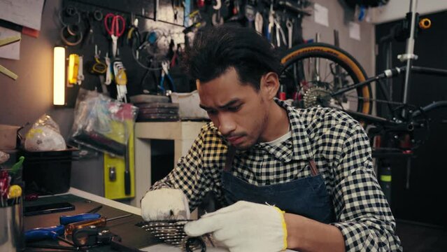 Professional young man repairing gear of bike wheel on the table in bicycle store. Maintenance and repair concept