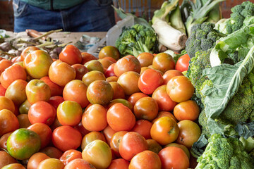 Fresh tomatoes on a country market stall alongside some fresh broccolis. Organic food. Balanced diet concept.