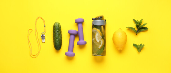 Sports bottle of cucumber lemonade with dumbbells and coach whistle on yellow background