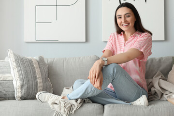 Young woman with stylish wristwatch sitting on sofa at home